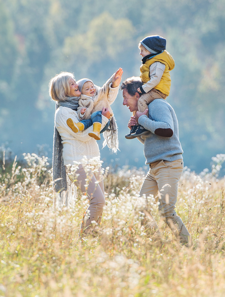 Small toddlers spending time with their grandfather and grandmother outside on a meadow in autumn.